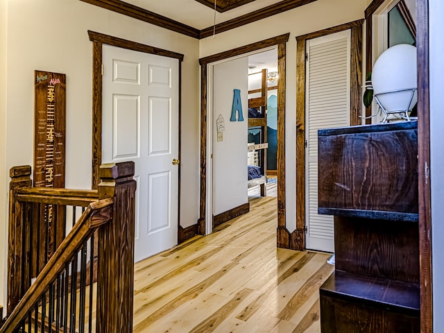 hall featuring an upstairs landing, light wood-type flooring, ornamental molding, and baseboards