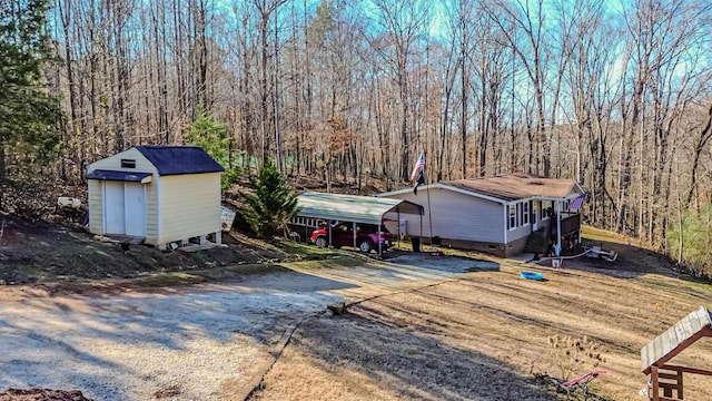 view of front facade featuring a wooded view, a storage unit, an outbuilding, a carport, and crawl space