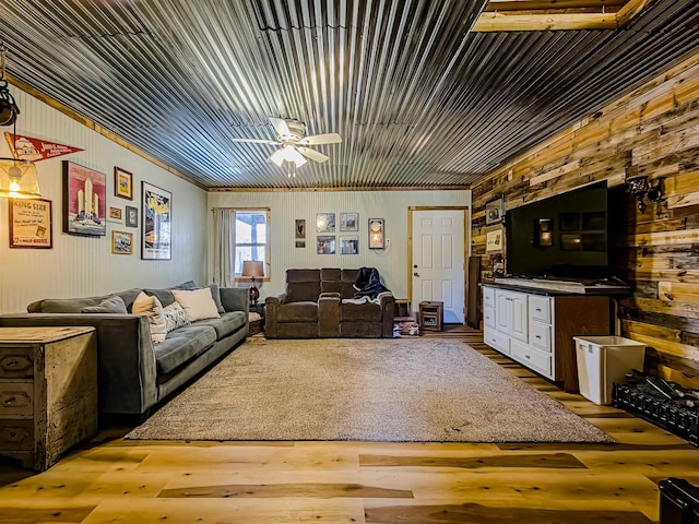 living room featuring wood finished floors, a ceiling fan, wooden walls, and crown molding