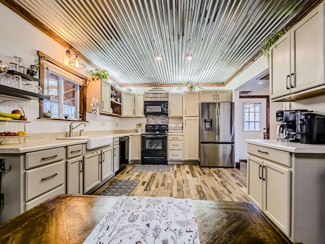 kitchen with open shelves, a sink, light countertops, black appliances, and light wood-type flooring