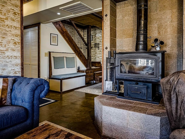 living area with visible vents, a wood stove, stairway, and finished concrete floors