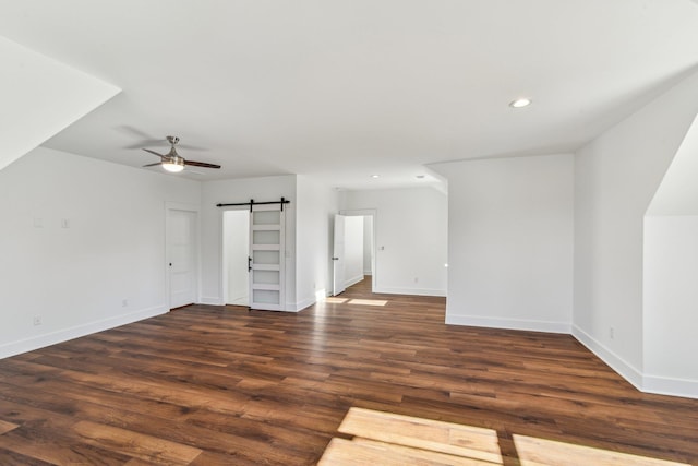 unfurnished living room with baseboards, a barn door, wood finished floors, and ceiling fan