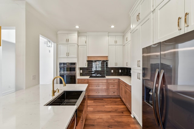 kitchen featuring recessed lighting, light stone counters, stainless steel fridge, a sink, and multiple ovens