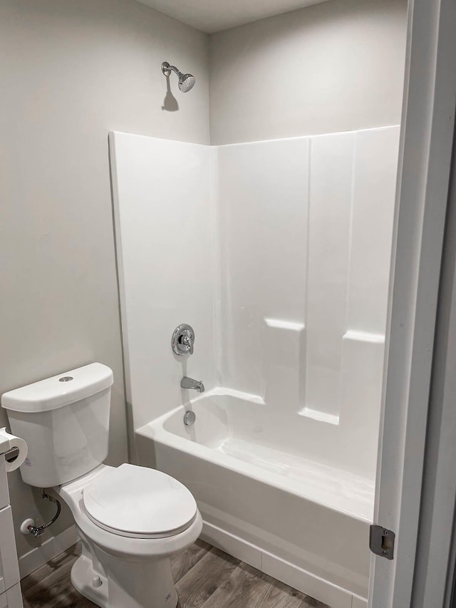 bathroom featuring wood finished floors, tub / shower combination, and toilet
