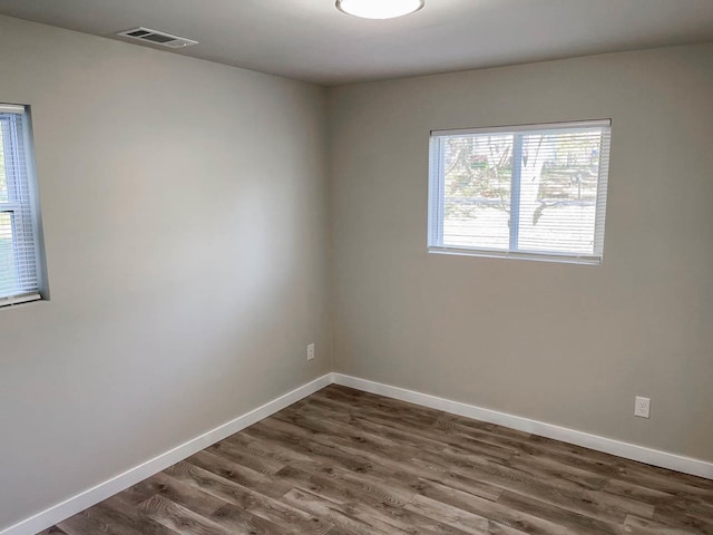 empty room with baseboards, visible vents, and dark wood finished floors
