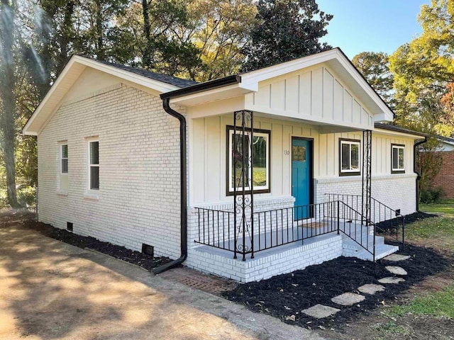 view of front of house with covered porch, board and batten siding, crawl space, and brick siding