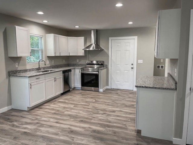 kitchen featuring wall chimney range hood, appliances with stainless steel finishes, a sink, recessed lighting, and stone counters