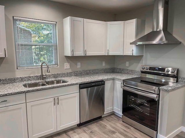 kitchen featuring wall chimney range hood, appliances with stainless steel finishes, a sink, light wood-style floors, and white cabinetry