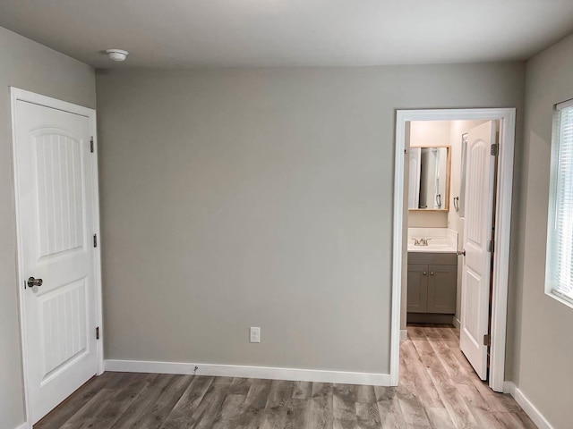 unfurnished bedroom featuring baseboards, a sink, wood finished floors, and ensuite bathroom