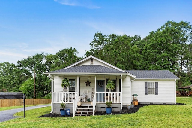 view of front of home featuring roof with shingles, fence, covered porch, and a front lawn