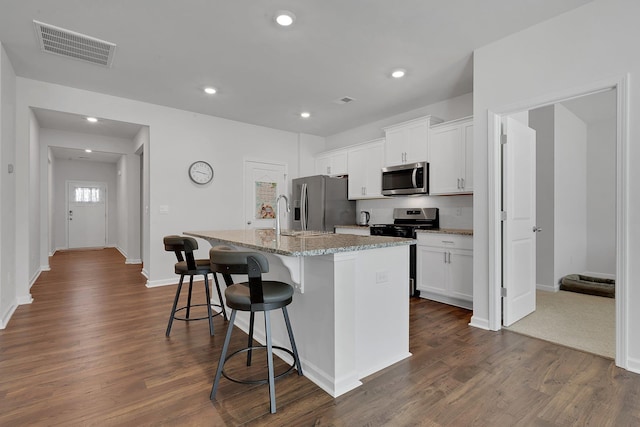 kitchen featuring a kitchen breakfast bar, an island with sink, stainless steel appliances, visible vents, and dark wood-style floors
