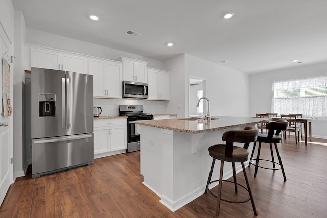 kitchen with visible vents, dark wood-type flooring, light stone counters, a sink, and stainless steel appliances