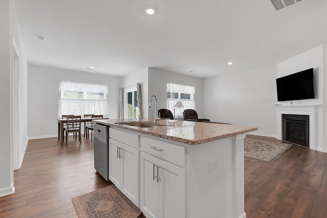 kitchen with stainless steel dishwasher, a sink, open floor plan, and light stone countertops