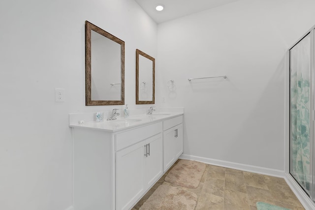 full bath featuring a sink, baseboards, walk in shower, and double vanity