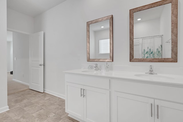 full bath featuring double vanity, a sink, a shower with door, and baseboards