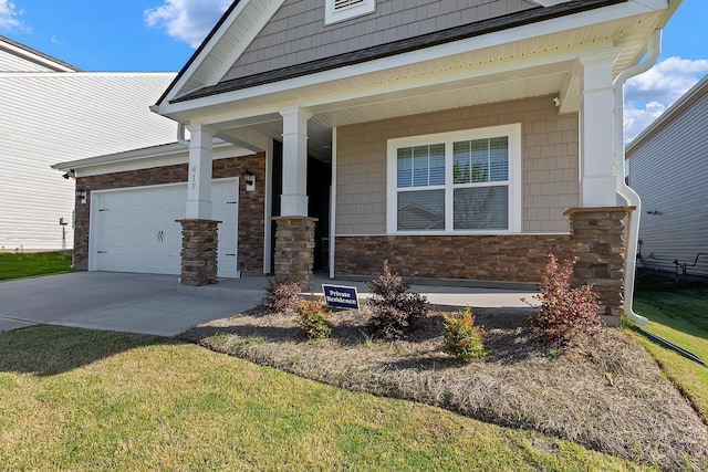 view of front of property with an attached garage, stone siding, a front yard, concrete driveway, and covered porch