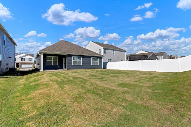 rear view of house with a lawn, a shingled roof, and fence