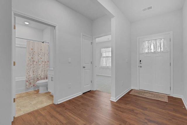 foyer entrance with baseboards, wood finished floors, and visible vents