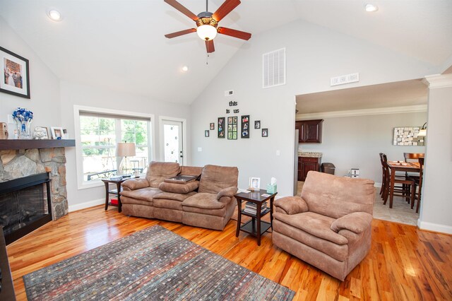 living room featuring ceiling fan, light wood finished floors, a fireplace, high vaulted ceiling, and visible vents