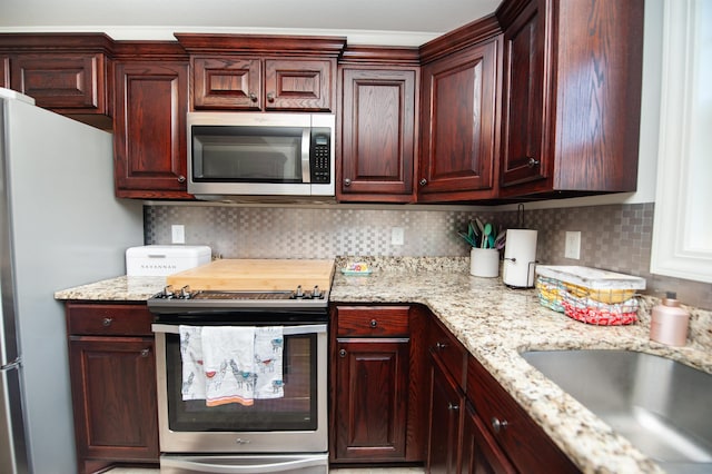 kitchen with stainless steel appliances, light stone countertops, a sink, and tasteful backsplash
