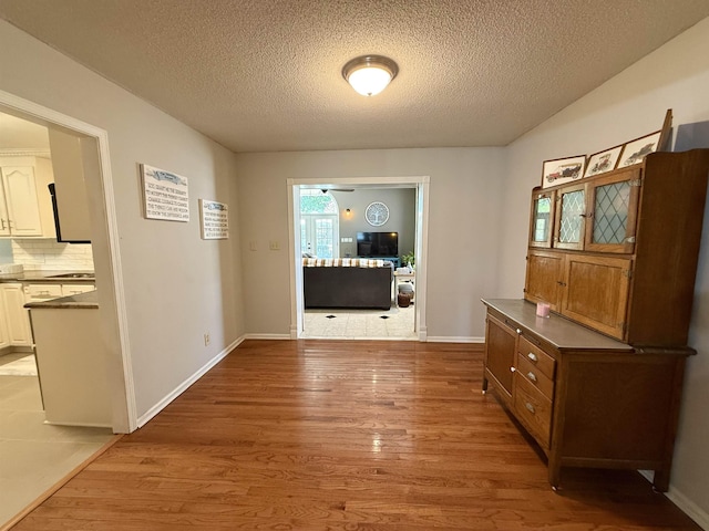 hall with baseboards, a textured ceiling, and wood finished floors