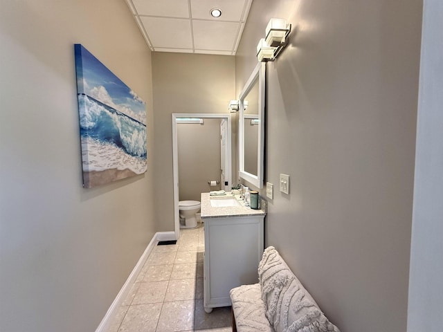 bathroom featuring vanity, baseboards, tile patterned floors, toilet, and a drop ceiling