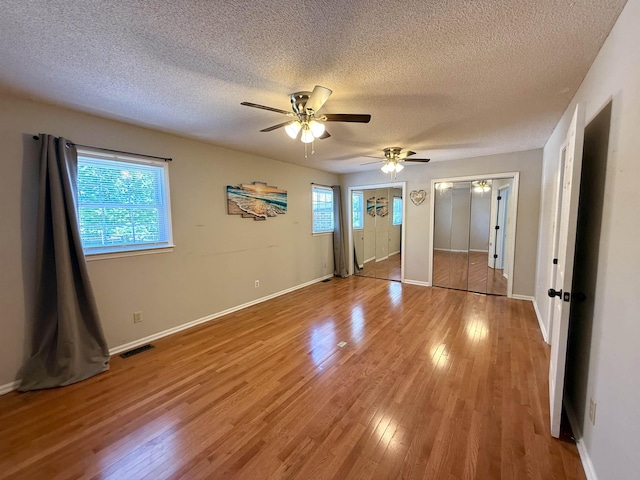 unfurnished bedroom featuring visible vents, a textured ceiling, multiple closets, and light wood-style flooring