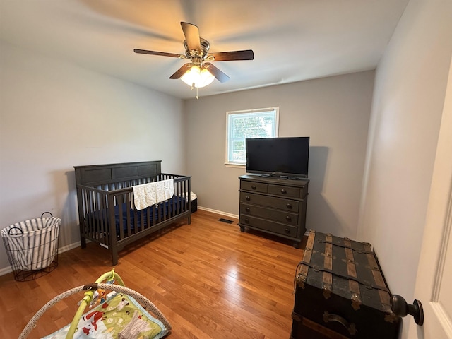 bedroom with light wood-type flooring, a ceiling fan, baseboards, and a nursery area