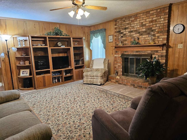 living room featuring a ceiling fan, a textured ceiling, a fireplace, wooden walls, and ornamental molding