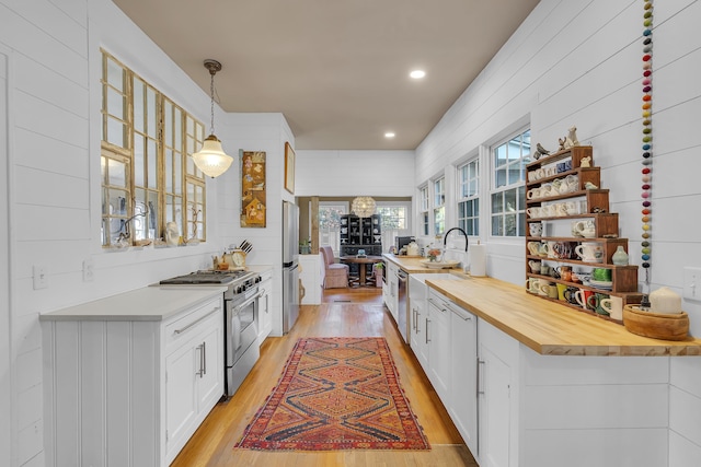 kitchen with white cabinets, appliances with stainless steel finishes, light wood finished floors, decorative light fixtures, and butcher block counters