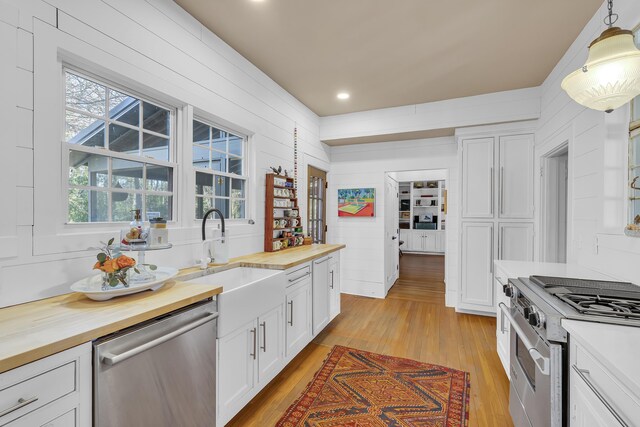 kitchen with white cabinets, a sink, butcher block countertops, light wood-style flooring, and stainless steel appliances