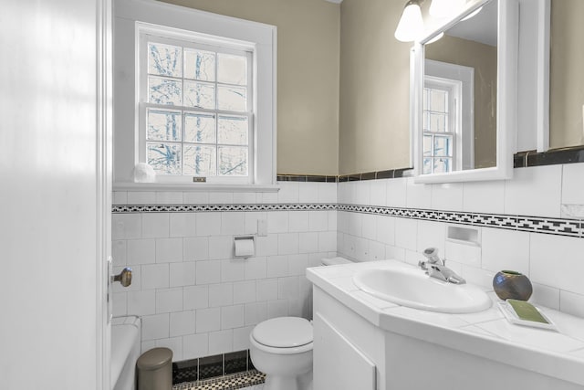 bathroom with a bathtub, tile walls, vanity, a wainscoted wall, and toilet