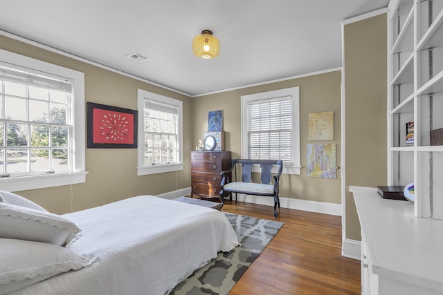 bedroom with baseboards, ornamental molding, wood finished floors, and visible vents