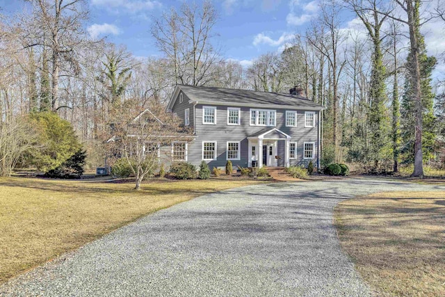 colonial-style house featuring covered porch, a chimney, driveway, and a front lawn
