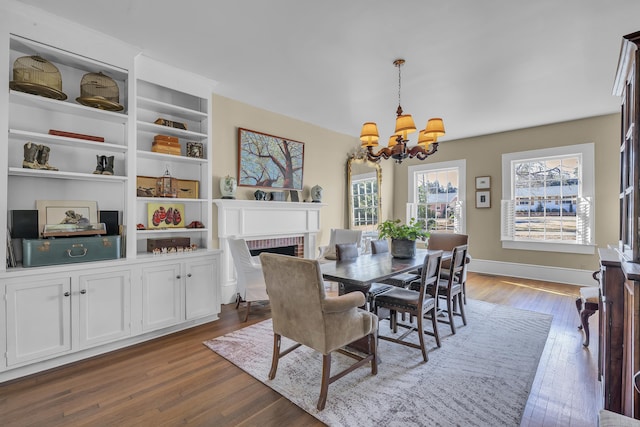 dining area with baseboards, a chandelier, dark wood-style floors, and a fireplace