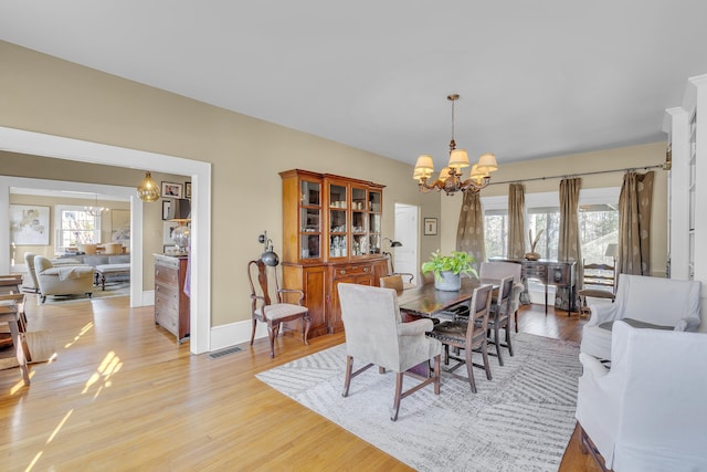 dining room featuring visible vents, light wood finished floors, baseboards, and a notable chandelier