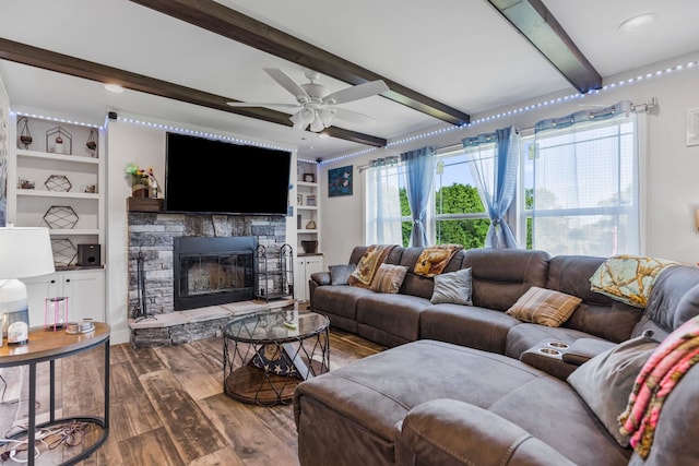 living room featuring beam ceiling, a ceiling fan, a stone fireplace, and wood finished floors