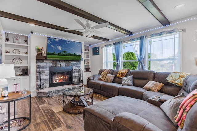 living area with ceiling fan, beam ceiling, a stone fireplace, and wood finished floors