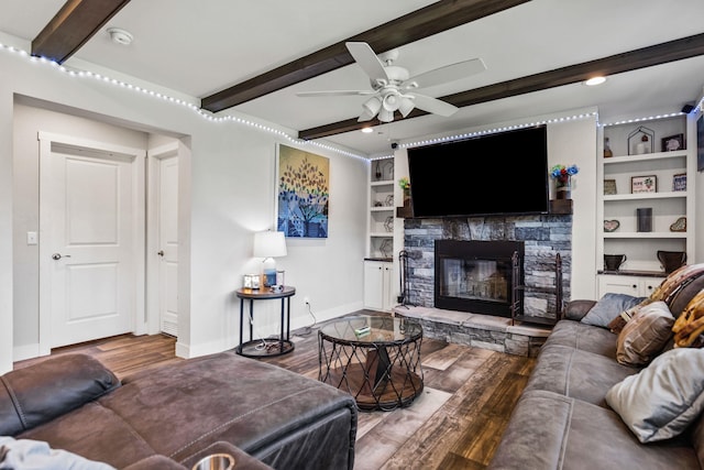 living area with beamed ceiling, baseboards, a stone fireplace, and wood finished floors