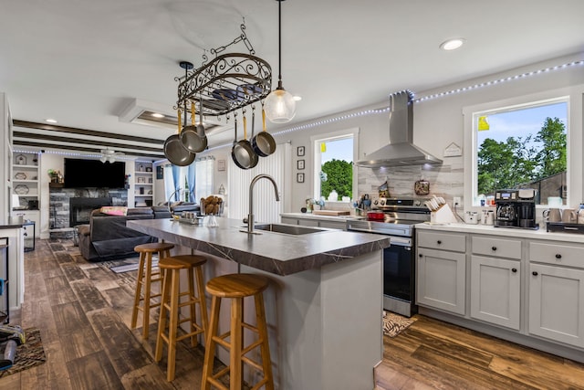 kitchen featuring electric range, dark countertops, open floor plan, wall chimney range hood, and a sink