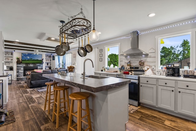 kitchen featuring wall chimney range hood, stainless steel electric range, dark countertops, a sink, and open floor plan
