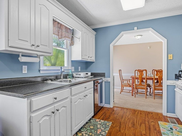 kitchen with dark countertops, a textured ceiling, white cabinets, a sink, and dishwasher