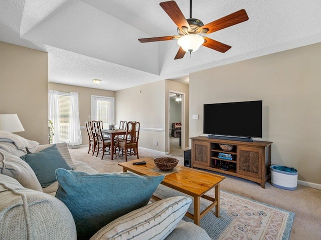 living area featuring baseboards, ceiling fan, light carpet, and a textured ceiling