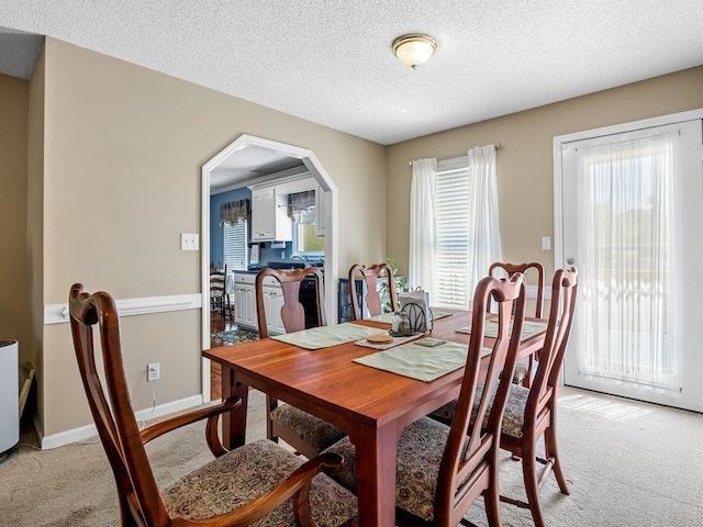 dining area featuring arched walkways, baseboards, a textured ceiling, and light colored carpet