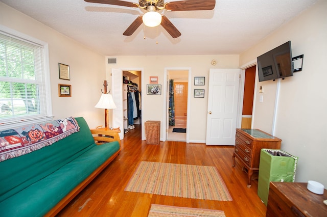 living area with visible vents, a ceiling fan, a textured ceiling, and wood finished floors