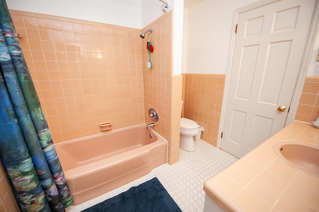 bathroom featuring a sink, toilet, shower / bathtub combination with curtain, a wainscoted wall, and tile walls