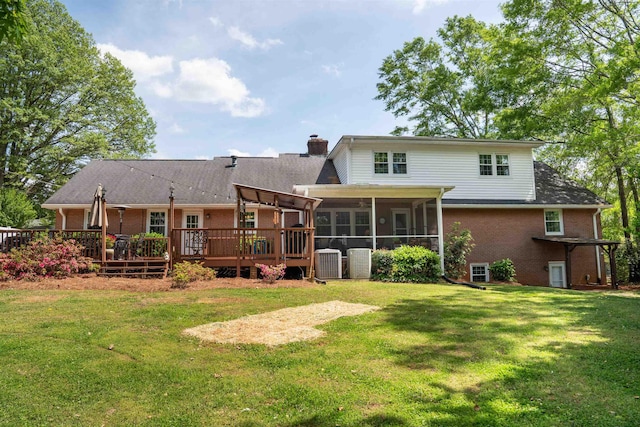 back of property with a chimney, a sunroom, brick siding, a lawn, and central air condition unit