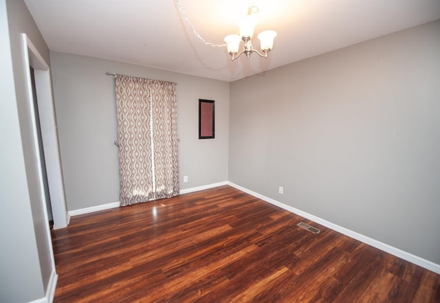 spare room with visible vents, baseboards, wood finished floors, and a chandelier