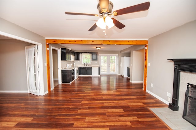unfurnished living room with a sink, dark wood finished floors, a ceiling fan, baseboards, and a fireplace with flush hearth