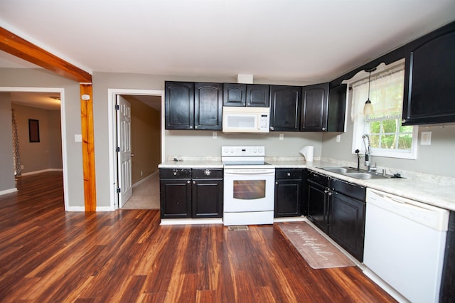 kitchen with a sink, white appliances, dark cabinetry, light countertops, and dark wood finished floors